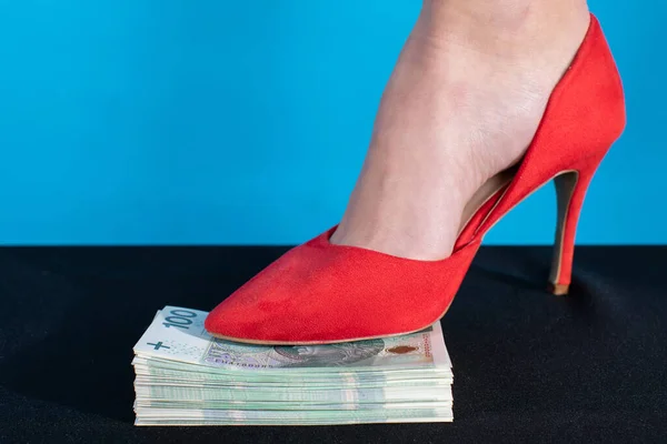 Managing hard rules in business and commerce through businesswomen. A female foot in a red high heel presses a bundle of money.