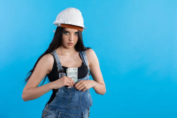 若い女性建設労働者は 彼女のズボンのポケット庭師に厚い紙幣の束を隠します 建設現場には建設マネージャーがいて大金を持ってる — ストック写真