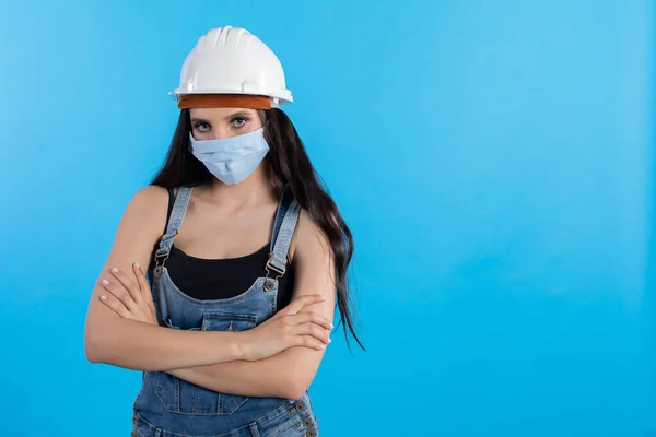 During the ongoing outbreak of the coronovirus, safety regulations are also tightened at the construction site to prevent it being seen. A young woman at a construction site wearing a helmet and a protective mask waits for orders from her superiors.