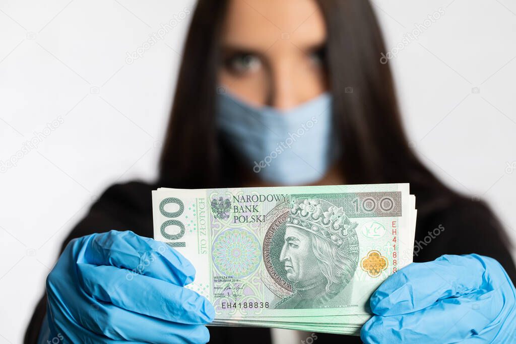 During the period of risk of infection with an infectious disease, it is necessary to use a face mask and rubber gloves. Businesswoman in a protective mask and protective gloves is holding a bundle of paper banknotes.