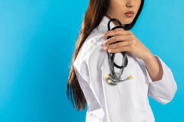 Doctor holds a stethoscope on his shoulder against the background of a medical apron.