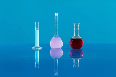 Cam şişelerdeki renkli kimyasallar temiz bir masanın üzerinde duruyor..