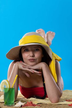 Kumsalda güneşlenirken, bir genç soğuk bir alkollü içecek içer..