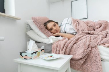 Hasta bir genç yatakta yatıyor. Yatağın önünde tabakları çeşitli tabletlerle dolu beyaz bir masa var..