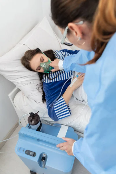 The teenager has a breathing ventilator connected. The doctor adjusts the respirator to give the right dose of oxygen.