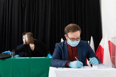 Adam, seçim kartının önündeki sandalyede oturuyordu. Bir aday seçer. Oy pusulasını doldurur.