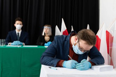 Genç seçmen sandık merkezinde bir sandalyede oturuyor ve Polonya cumhurbaşkanı için oy pusulasını dolduruyor..