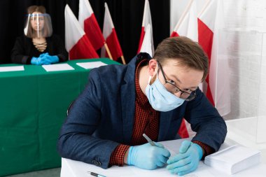 Genç seçmen sandık merkezinde bir sandalyede oturuyor ve Polonya cumhurbaşkanı için oy pusulasını dolduruyor..