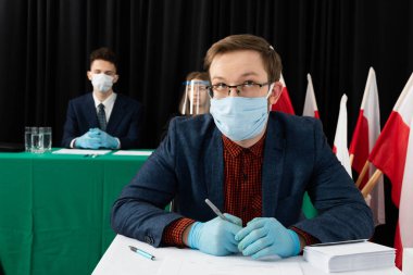 Genç seçmen sandık merkezinde bir sandalyede oturuyor ve Polonya cumhurbaşkanı için oy pusulasını dolduruyor..