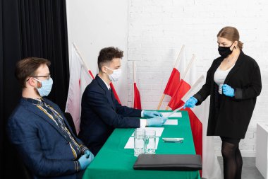 Genç bir genç oy pusulasının çıkarılmasını bekliyor. Erkek seçim komisyonu sorun için belgeler hazırlıyor.