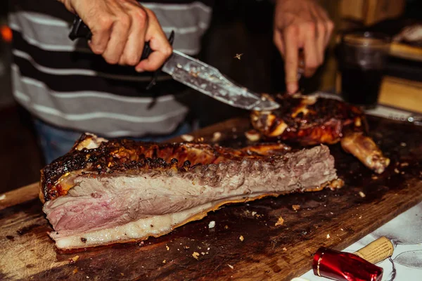 Chef mão corta pedaço de porco grelhado em bifes com faca. Porco leiteiro tradicional cozinhado na grelha de carvão. O porquinho é assado inteiro em uma fogueira. Porco orgânico na saliva . — Fotografia de Stock