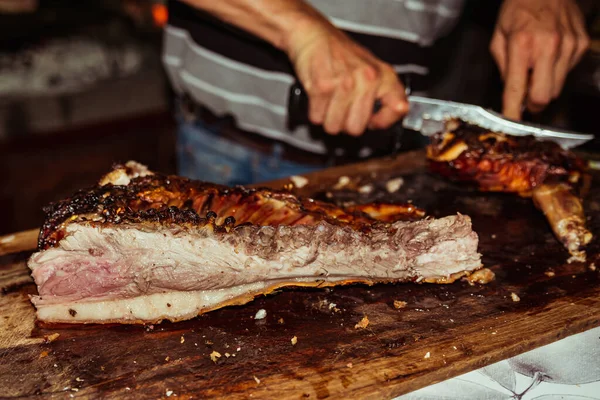 Chef mão corta pedaço de porco grelhado em bifes com faca. Porco leiteiro tradicional cozinhado na grelha de carvão. O porquinho é assado inteiro em uma fogueira. Porco orgânico na saliva . — Fotografia de Stock