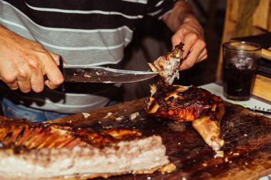 Şefin eli bıçakla ızgara domuz eti kesiyor. Kömür ızgarasında geleneksel domuz eti. Küçük domuz açık ateşte kavruluyor. Tükürüğünde organik domuz.