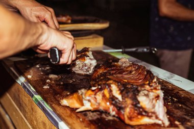Şefin eli bıçakla ızgara domuz eti kesiyor. Kömür ızgarasında geleneksel domuz eti. Küçük domuz açık ateşte kavruluyor. Tükürüğünde organik domuz.