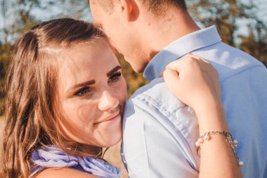 Saman tarlasında birbirine sarılıp gülümseyen genç çifti yakından çek. Erkek kadına sıkıca sarılır. Açık havada, yazın poz veren güzel, romantik bir çiftin portresi.