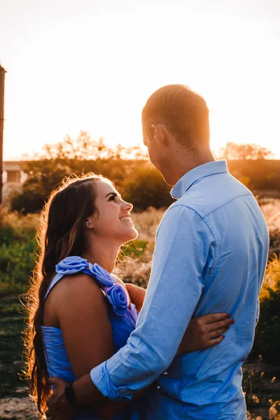 Pareja joven enamorada se abraza al atardecer en medio de un puente en construcción. La mujer y el hombre se miran. Retrato exterior de hermosa pareja romántica en ropa ligera en los rayos del sol —  Fotos de Stock