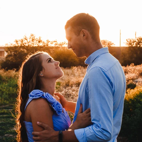 Pareja joven enamorada se abraza al atardecer en medio de un puente en construcción. La mujer y el hombre se miran. Retrato exterior de hermosa pareja romántica en ropa ligera en los rayos del sol —  Fotos de Stock