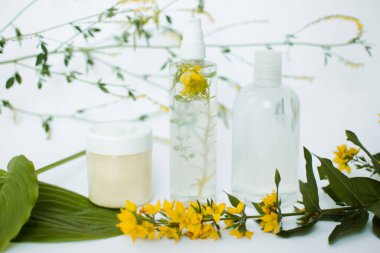 Yeşil yapraklı kozmetik şişeleri ve beyaz arka planda sarı çiçekler. Bitkisel malzemeli doğal organik kozmetik. Marka modellemesi için etiket. Güzellik, sağlık ve cilt bakımı kavramı