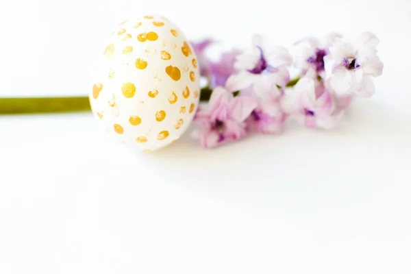 Hand painted egg with gold dots and violet phlox lying in line on white. Happy Easter background, greeting card. Copy space