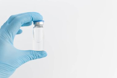 Doktorlar mavi lastik eldiveni, mavi kapaklı ilaç şişesini ve gri arka planda temiz sıvıyı tutarak teslim ediyorlar. Coronavirus aşısı geliştirme. 2019 nCoV sıvı ilaç, virüs panzehiri. Boşluğu kopyala