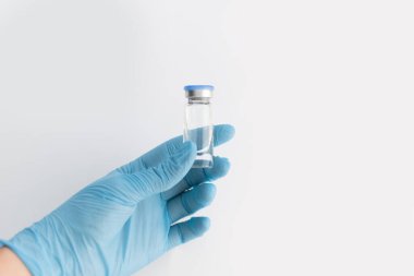 Doktorlar mavi lastik eldiveni, mavi kapaklı ilaç şişesini ve gri arka planda temiz sıvıyı tutarak teslim ediyorlar. Coronavirus aşısı geliştirme. 2019 nCoV sıvı ilaç, virüs panzehiri. Boşluğu kopyala