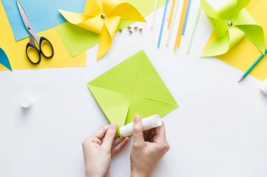 Evde çocuklarla kağıt yeşili yel değirmeni oyuncağı yapmayı. Adım adım talimatlar. Eller DIY yaz projesi yapıyor. Üst Manzara. Altıncı adım. Ortaya çıkan üçgenin sağ köşesine yapıştırıcı uygula
