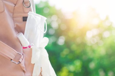 Pembe el dezenfektanı, beyaz yüz tıbbi koruyucu maske ve deri sırt çantasının içinde yeşil arka planda bulanık plastik eldivenler. Yeni normal. Refah ve önleme kavramı