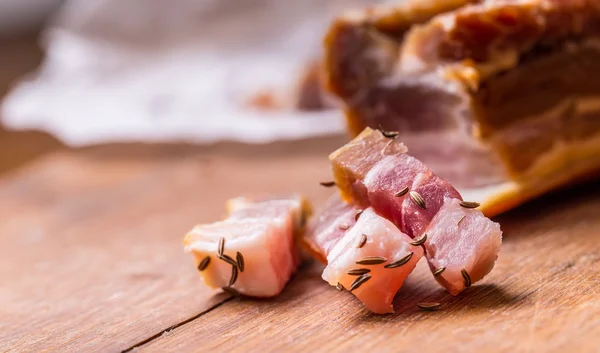 Fette di pancetta affumicata cruda su tavola di legno con cumino ed erbe aromatiche — Foto Stock