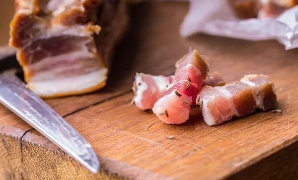 Fette di pancetta affumicata cruda su tavola di legno con cumino ed erbe aromatiche — Foto Stock