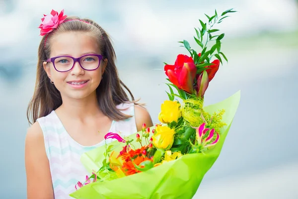 Beautiful little girl posing with a large bouquet of flowers. Girl with braces and glasses — Stock Photo, Image