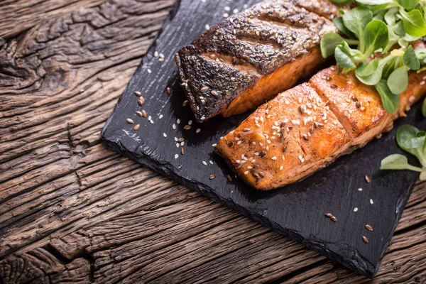 Laxfiléer. Grillad lax, sesam frön ört decorationon på vintage pan eller svart skiffer styrelse. fisken grillas på ett gammalt träbord. Studio skott — Stockfoto