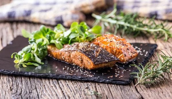 Salmon fillets. Grilled salmon, sesame seeds herb decorationon on vintage pan or black slate board. fish roasted on an old wooden table.Studio shot