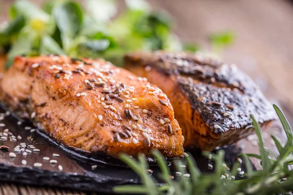 Salmon fillets. Grilled salmon, sesame seeds herb decorationon on vintage pan or black slate board. fish roasted on an old wooden table.Studio shot — Stock Photo, Image