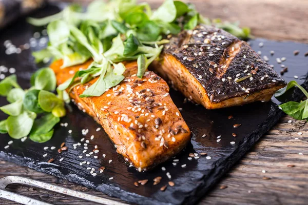 Laxfiléer. Grillad lax, sesam frön ört decorationon på vintage pan eller svart skiffer styrelse. fisken grillas på ett gammalt träbord. Studio skott — Stockfoto