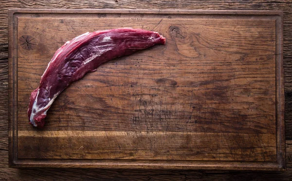 Raw beef tenderloin steak on a cutting board with rosemary pepper salt in other positions