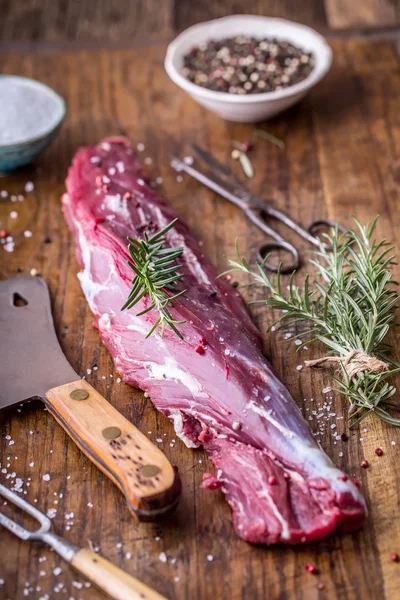 Raw beef tenderloin steak on a cutting board with rosemary pepper salt in other positions