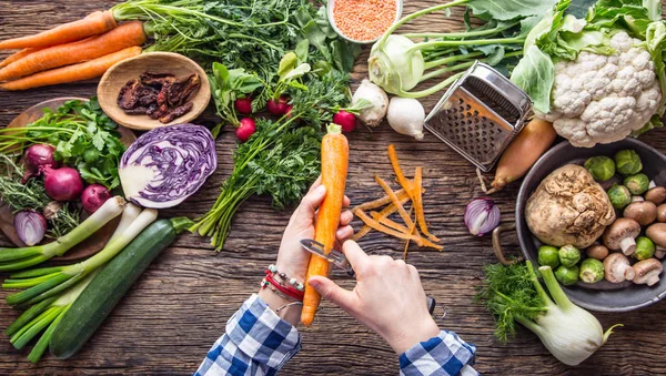 Las manos de las mujeres están cortando zanahoria en una tabla de madera cerca de las verduras — Foto de Stock
