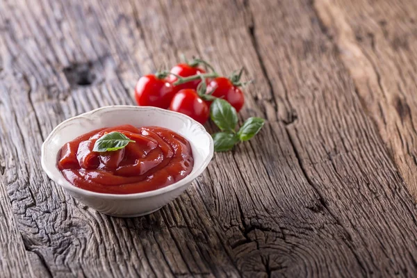 Ketchup o salsa de tomate en tazón blanco y tomates cherry en mesa de madera — Foto de Stock