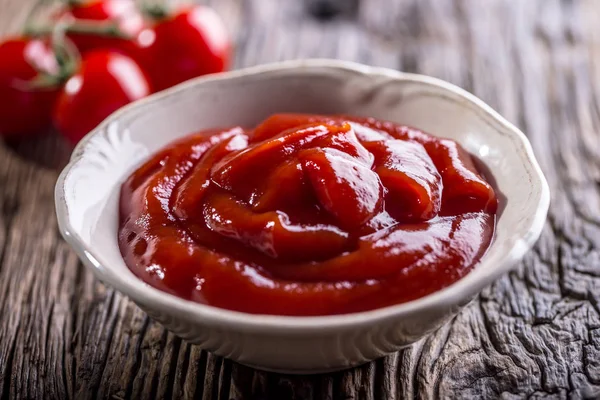 Кетчуп или томатный соус в белой миске и помидоры черри на деревянном столе — стоковое фото