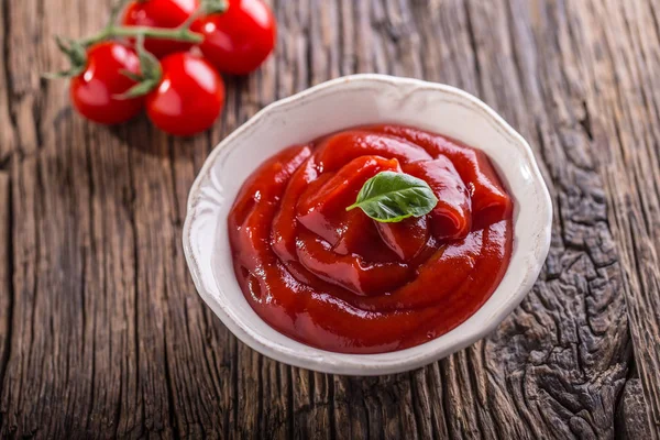 Ketchup o salsa de tomate en tazón blanco y tomates cherry en mesa de madera — Foto de Stock