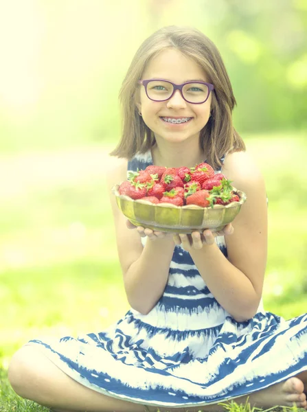 Linda niña con un tazón lleno de fresas frescas. Pre - adolescente con gafas y dientes - aparatos dentales — Foto de Stock