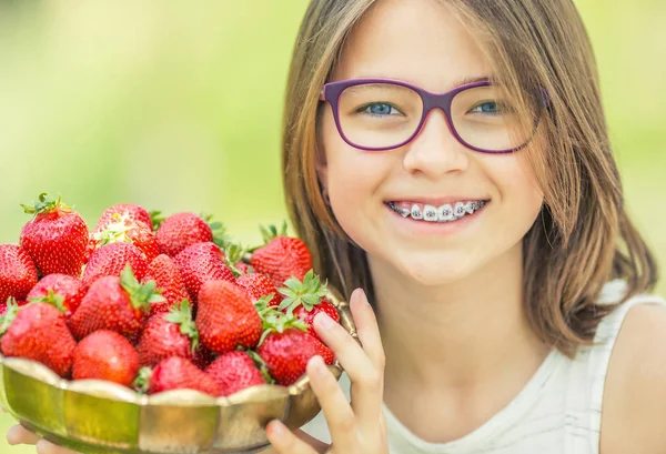 Linda niña con un tazón lleno de fresas frescas. Pre - adolescente con gafas y dientes - aparatos dentales — Foto de Stock