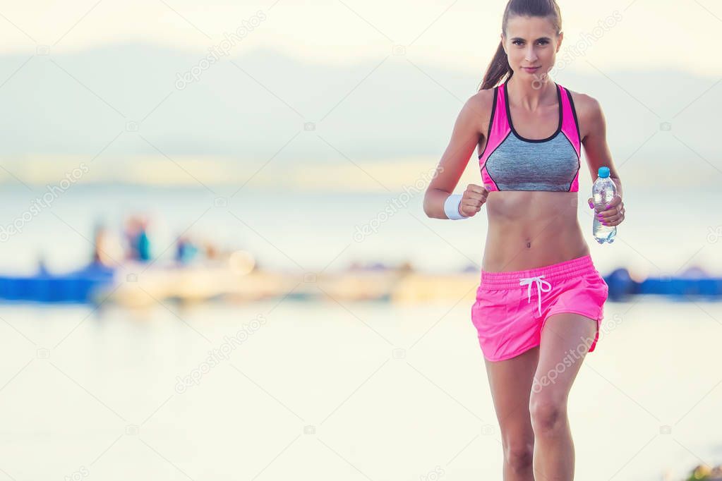 Attractive young woman running on the beach with bottle of water