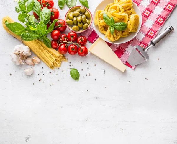 Cocina italiana e ingredientes en mesa de hormigón blanco. Espaguetis Tagliatelle aceitunas aceite de oliva tomates queso parmesano ajo pimienta y hojas de albahaca y mantel a cuadros. Espacio libre para su texto o información — Foto de Stock