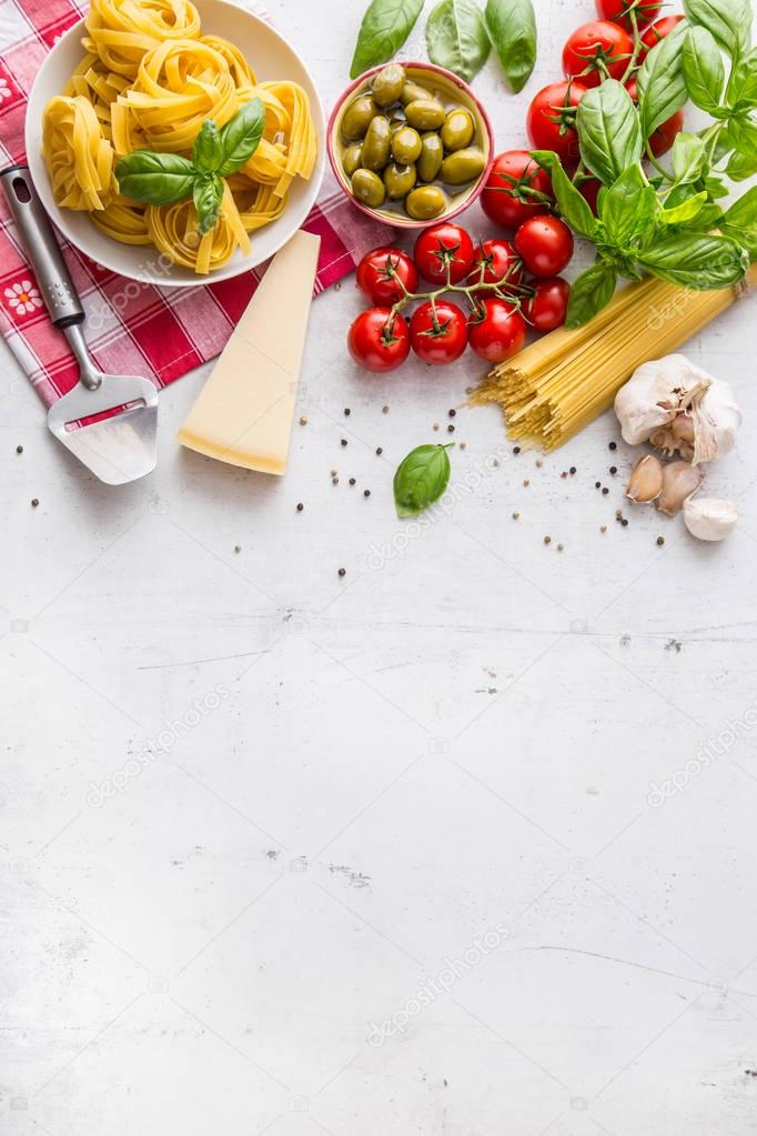 Italian food cuisine and ingredients on white concrete table. Spaghetti Tagliatelle olives olive oil tomatoes parmesan cheese garlic pepper and basil leaves and checkered tablecloth. Free space for your text or information