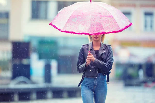 Attraente giovane donna con ombrello rosa sotto la pioggia e forte vento. Ragazza con ombrello in autunno . — Foto Stock