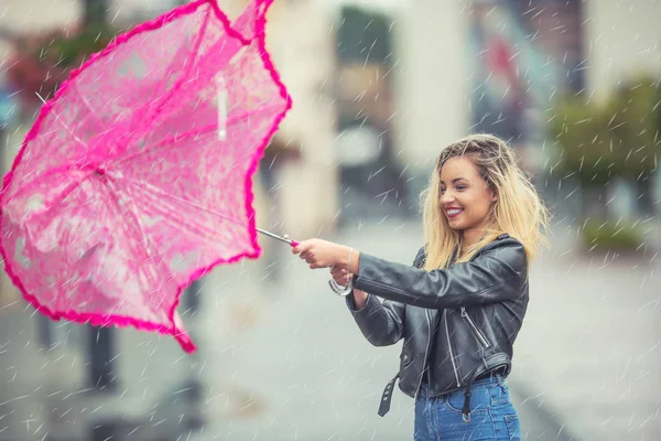 Attractive young woman with pink  umbrella in the rain and strong wind. Girl with umbrella in autumn weather.