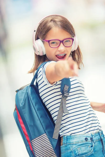 Skolflicka med väska, ryggsäck. Porträtt av modern glad tonåring skolflicka med väska ryggsäck hörlurar och tablett. Flicka med tandställning och glasögon — Stockfoto