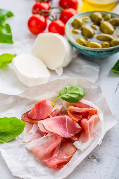 Prosciutto olijven olijfolie mozzarella kaas tomaten basilicum - ingrediënten Italiaanse of mediterrane keuken — Stockfoto