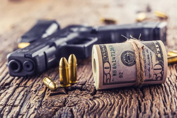 Пистолет и деньги. Пистолетные пули калибра 9 мм разбросаны по деревенскому дубовому столу — стоковое фото